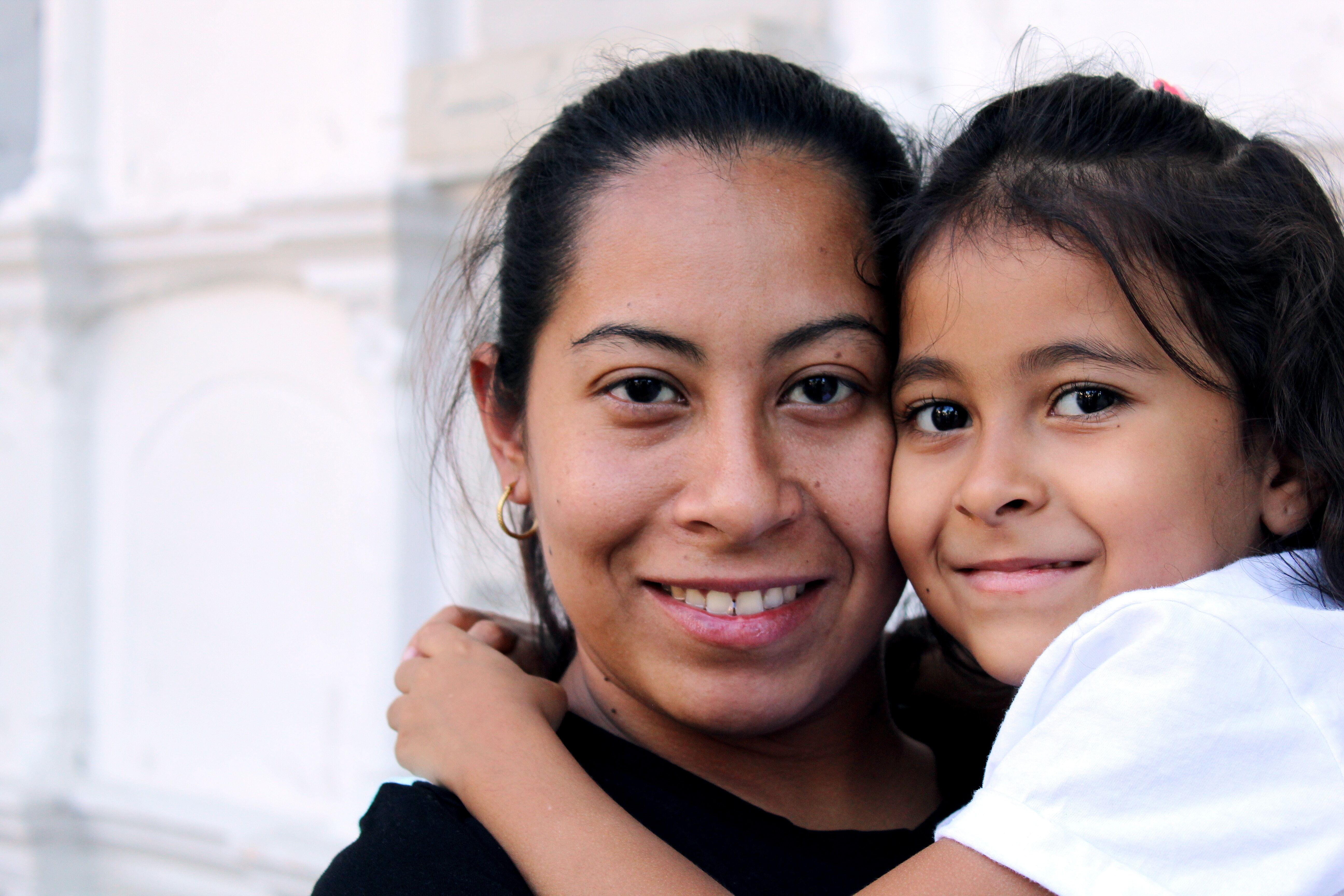 Adult with dark hair is smiling and holding a small child with dark hair who is smiling