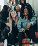 Seven young women sit on a decorated stairway, smiling and talking