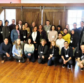 Group photo of conference attendees posing indoors on wood floors in front of large rustic sliding barn doors.