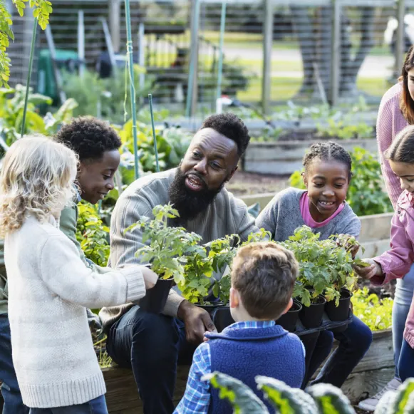 A man in a garden talks about the plant he is holding with the children gathered around him