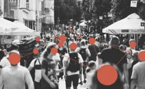 Black-and-white photo of a crowded street with red dots and connecting lines overlay, representing networks, data, and community connections