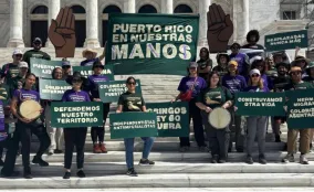 Group of activists on building steps hold signs advocating for Puerto Rican land rights, solidarity, and self-determination.