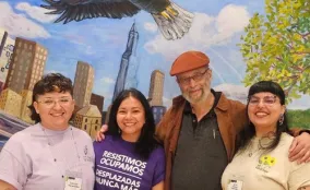 Four smiling people stand in front of a mural of a skyline and an eagle