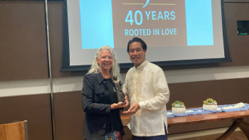 Two people smile holding a bronze statuette award beneath a screen reading "SJF 40 Years Rooted in Love" at the award event.