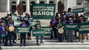 Group of activists on building steps hold signs advocating for Puerto Rican land rights, solidarity, and self-determination.