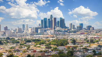 Los Angeles skyline with downtown high-rises rising above residential neighborhoods under a blue sky with scattered clouds.