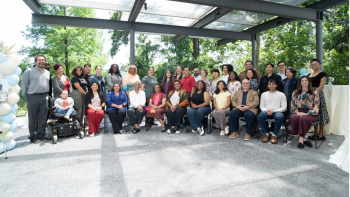 Group of staff members posing together at an outdoor gathering beneath a covered pavilion surrounded by trees.