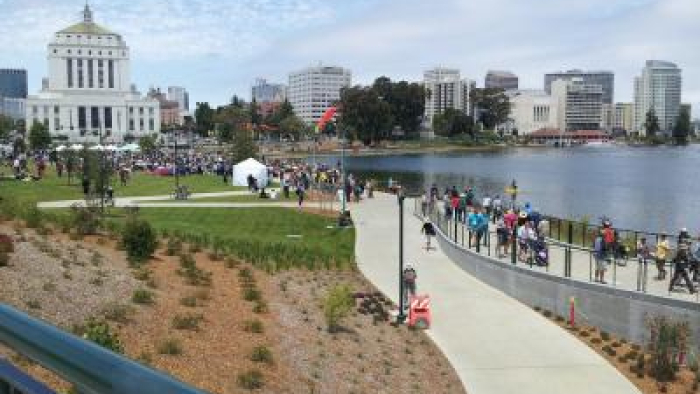 Crowds gather along Lake Merritt in Oakland near the white courthouse and city skyline on a sunny day.