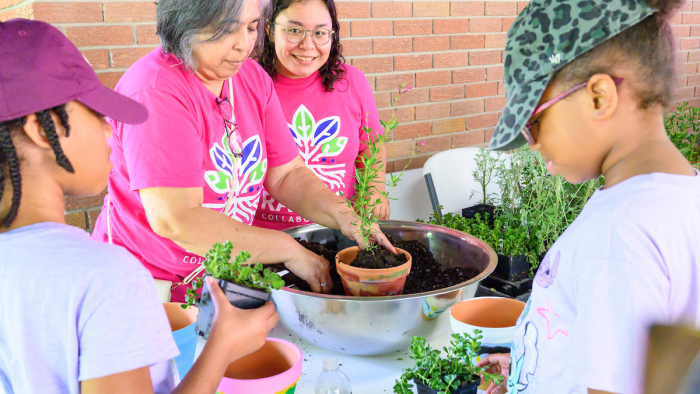 Two adults and two children pot herbs together during a hands-on community gardening activity.