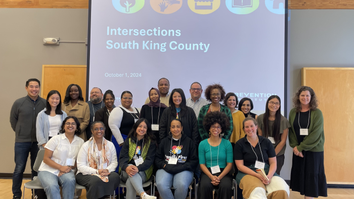 Group of community partners posing in front of Intersections South King County presentation screen at an October 2024 convening.